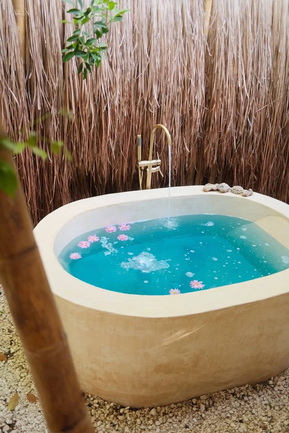 Outdoor stone star bath with turquoise water and flowers under open sky at Mauna Tulum